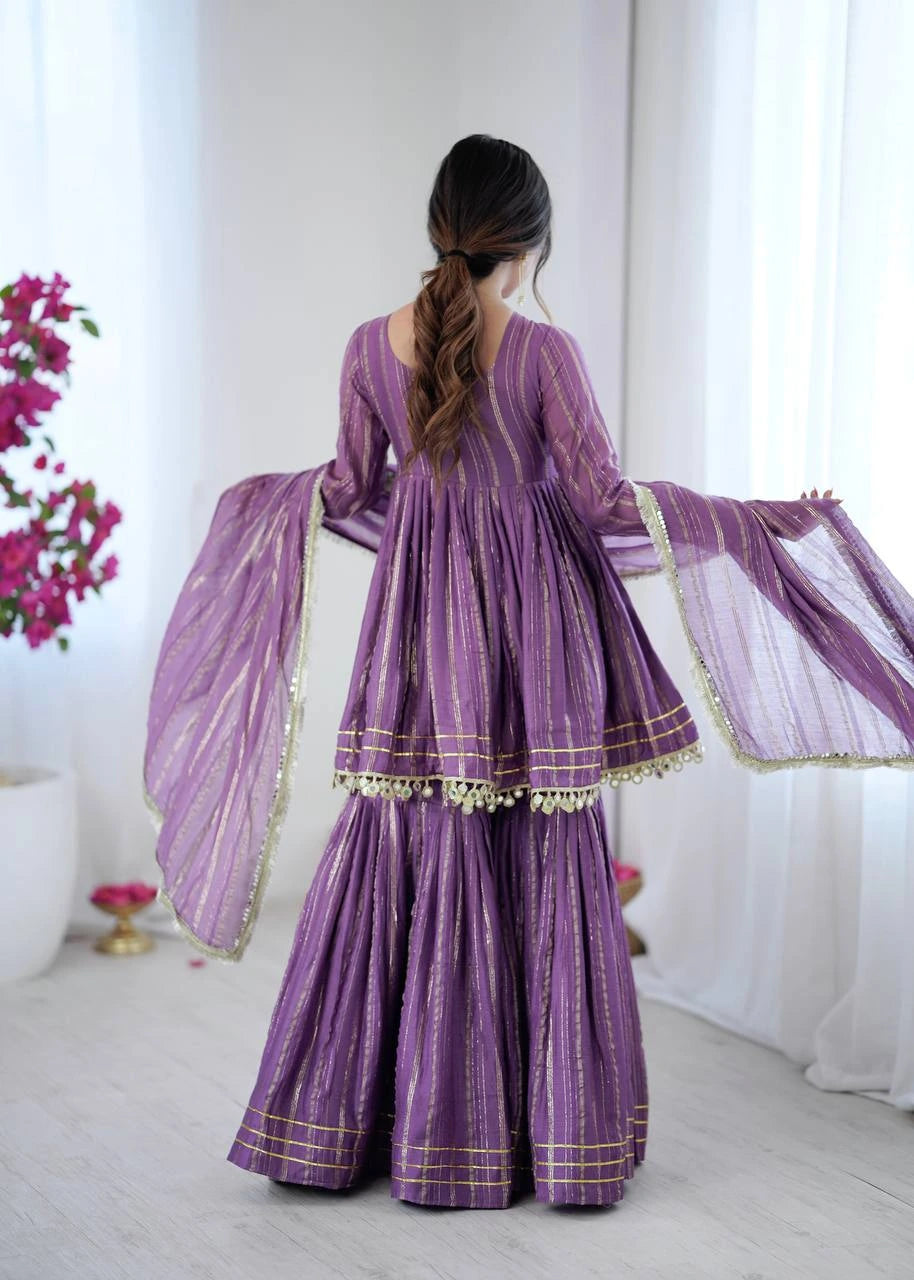 Person wearing a purple traditional outfit with gold details in a bright room.